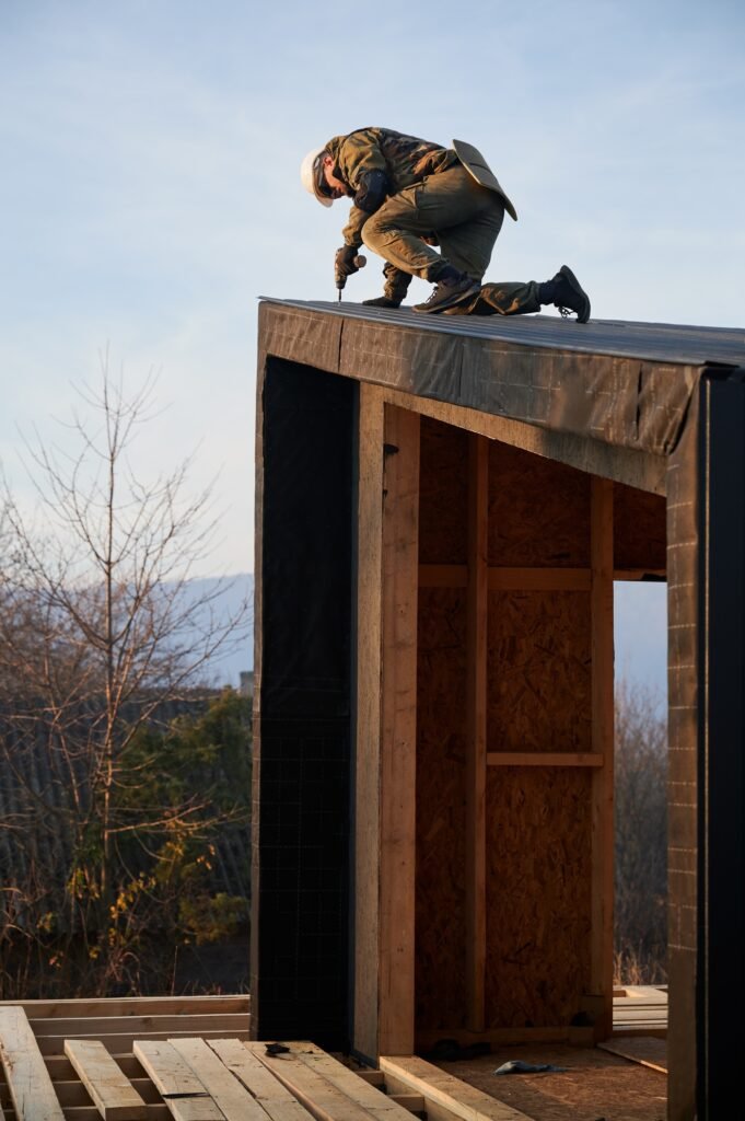 Builder installing corrugated iron sheet used as facade of future wooden frame house.